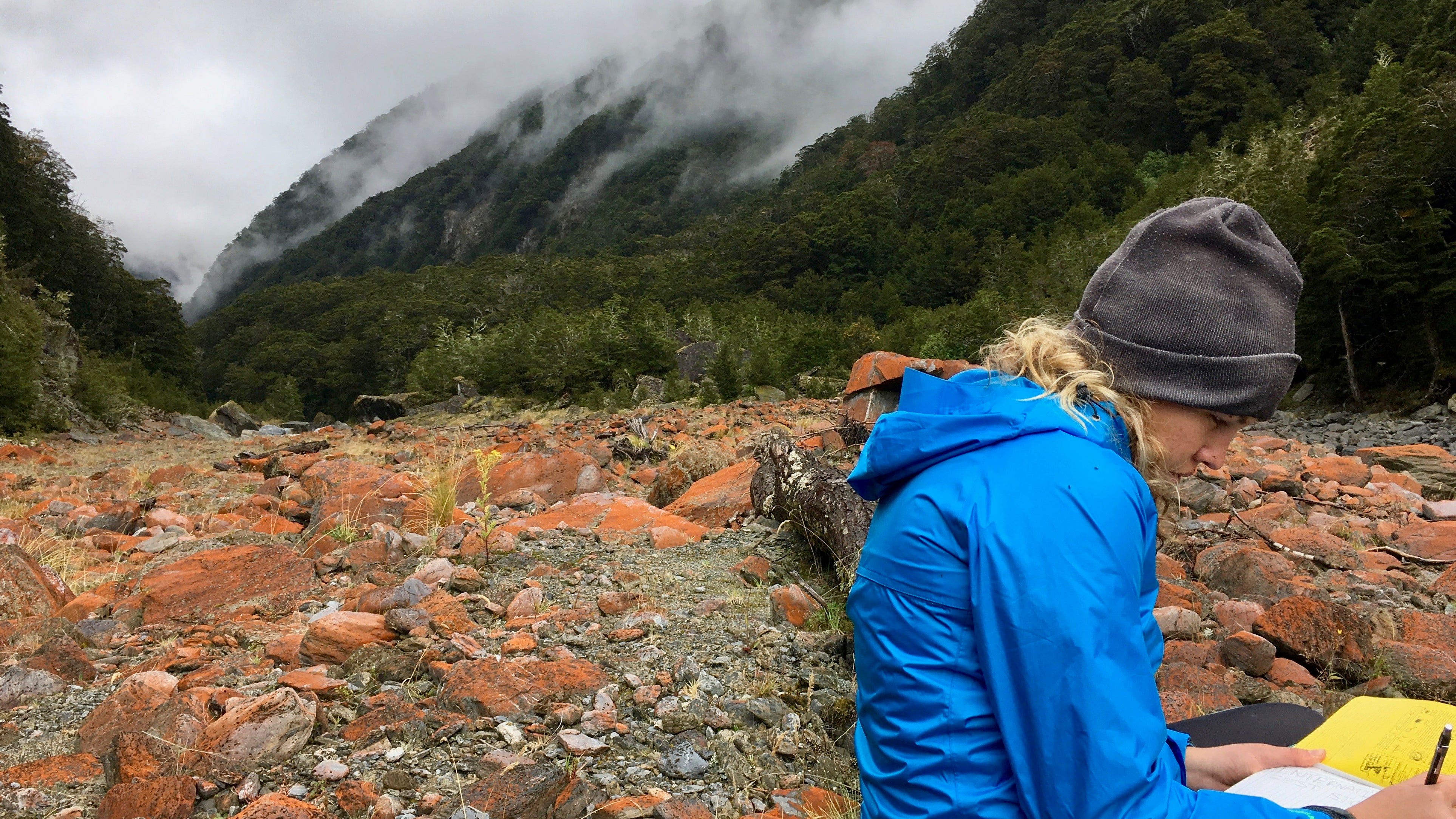 Student writes in notebook, sitting outdoors.