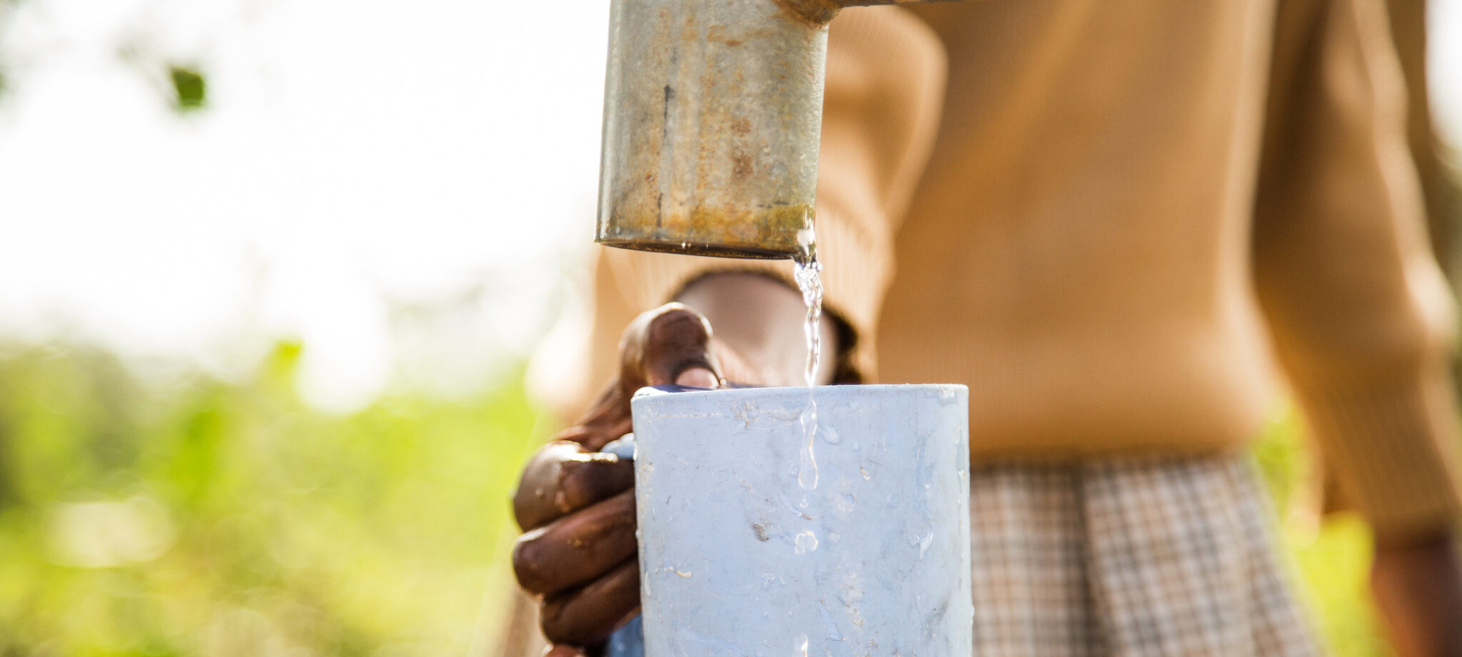 Hand holding cup of water under faucet outside