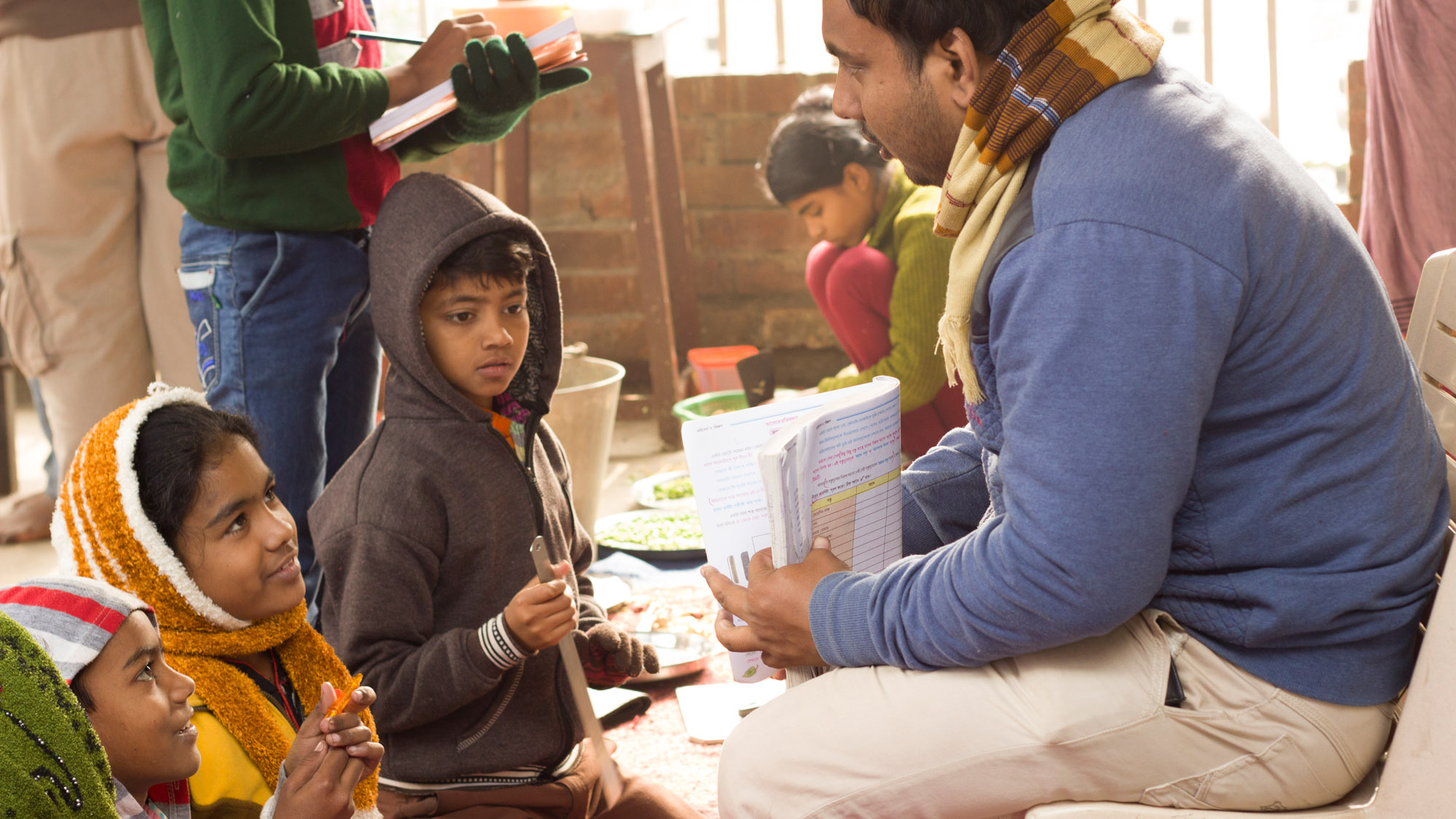 A teacher in a village in India explains to his students while holding an exercise book.